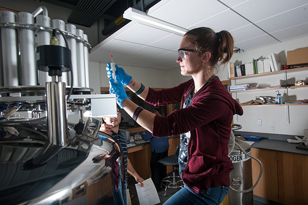 a BSU chemistry student working with a large piece of equipment with another student and a faculty member