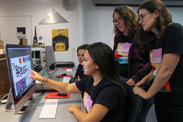 four students gathered around a computer looking at a cover design for The Bridge