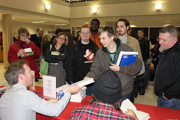 A group of students standing in front of of a table getting books autographed by visiting author Paul Murray