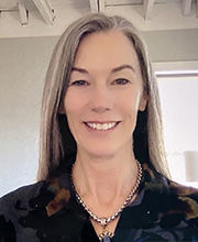 headshot photo of Christy Lyons Graham smiling with long straight gray hair wearing dark colored floral v-neck collared top