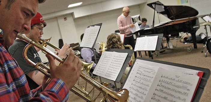 Jazz band class with students playing horns in the foreground, students playing saxophones, a professor, a piano and drum set in the background.  