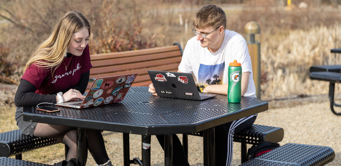 2 students sitting at an outdoor table studying with laptops open