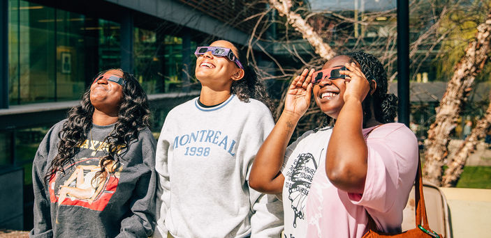 Three students look at the sun while wearing eclipse glasses.