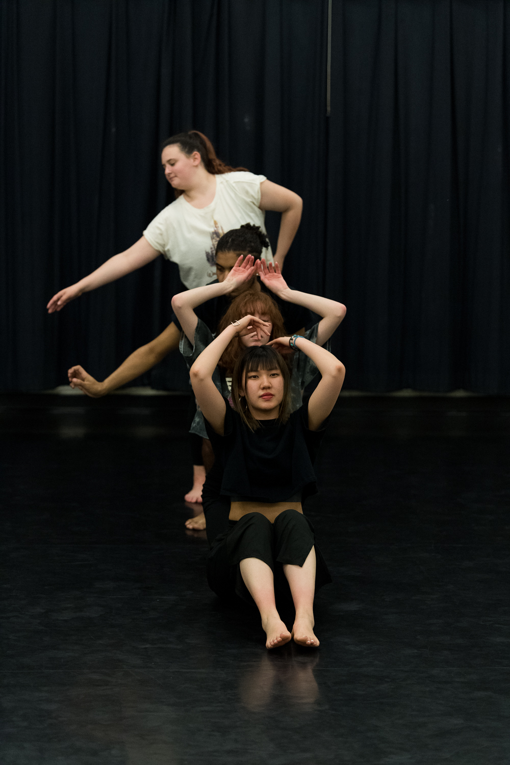 Four students dance in front of a black curtain