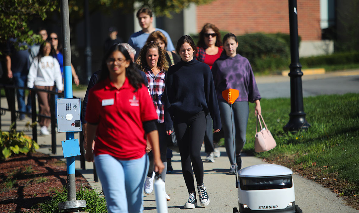 A group of prospective BSU students following a tour guide and a food delivery robot