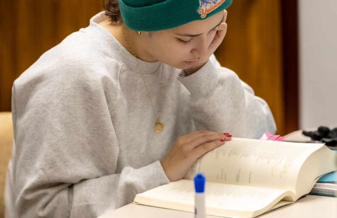 A student wearing a teal beanie studies an open book