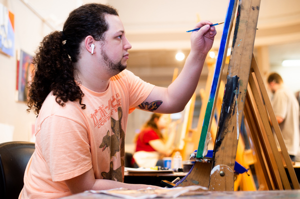 a BSU student sitting at an easel painting with other students painting at easels in the background