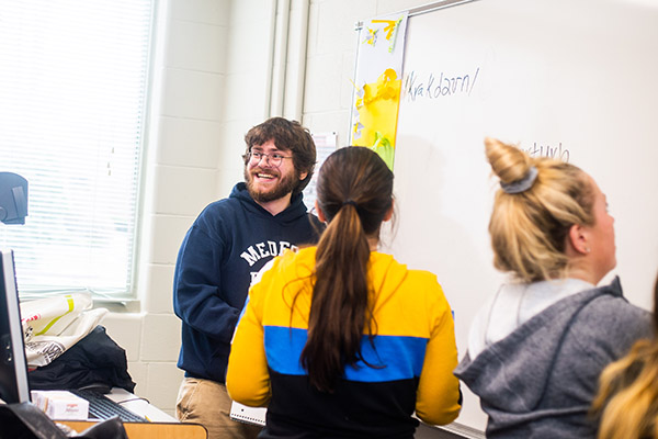 students in phonetics class working at the white board while one looks toward the classroom smiling