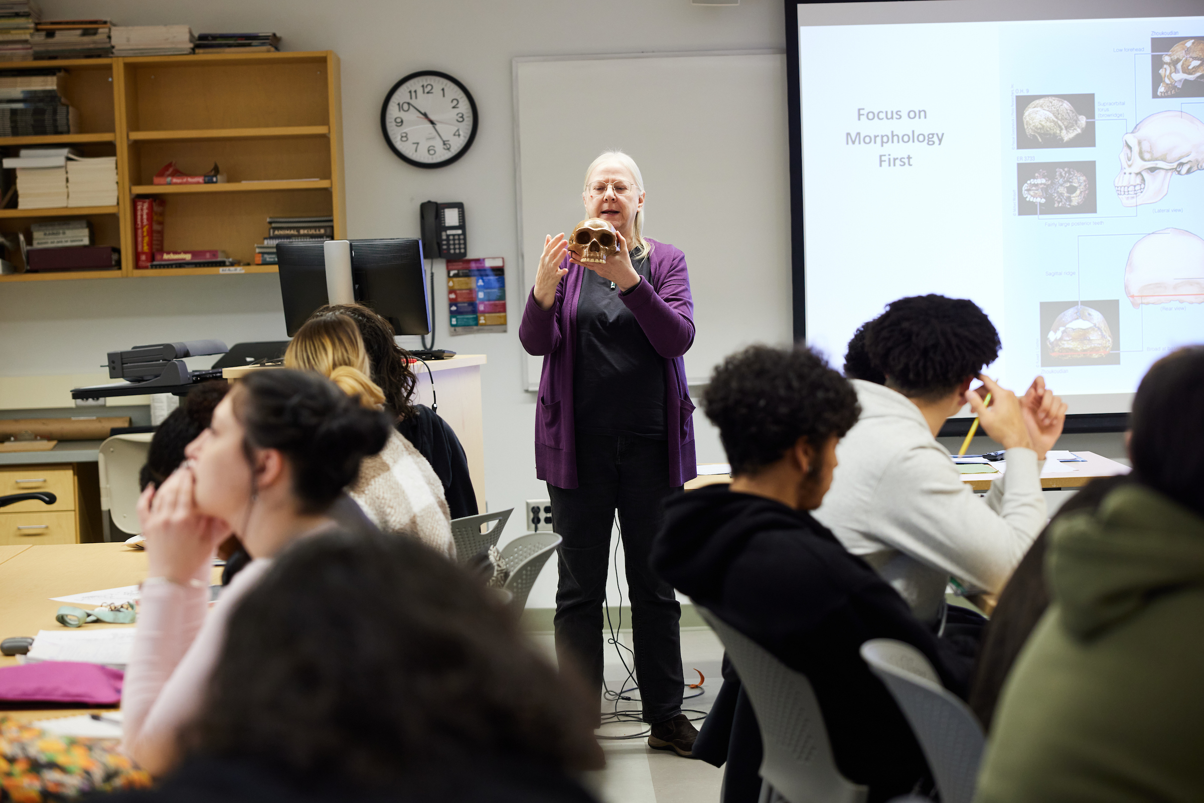 Dr. Ellen Ingmanson speaking at front of class while holding a skull next to a projector screen