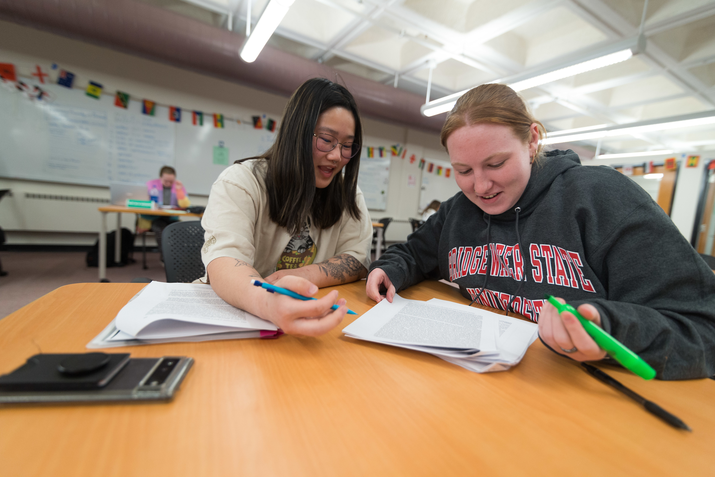 2 female students sit at a table in the Academic Achievement Center working together over papers