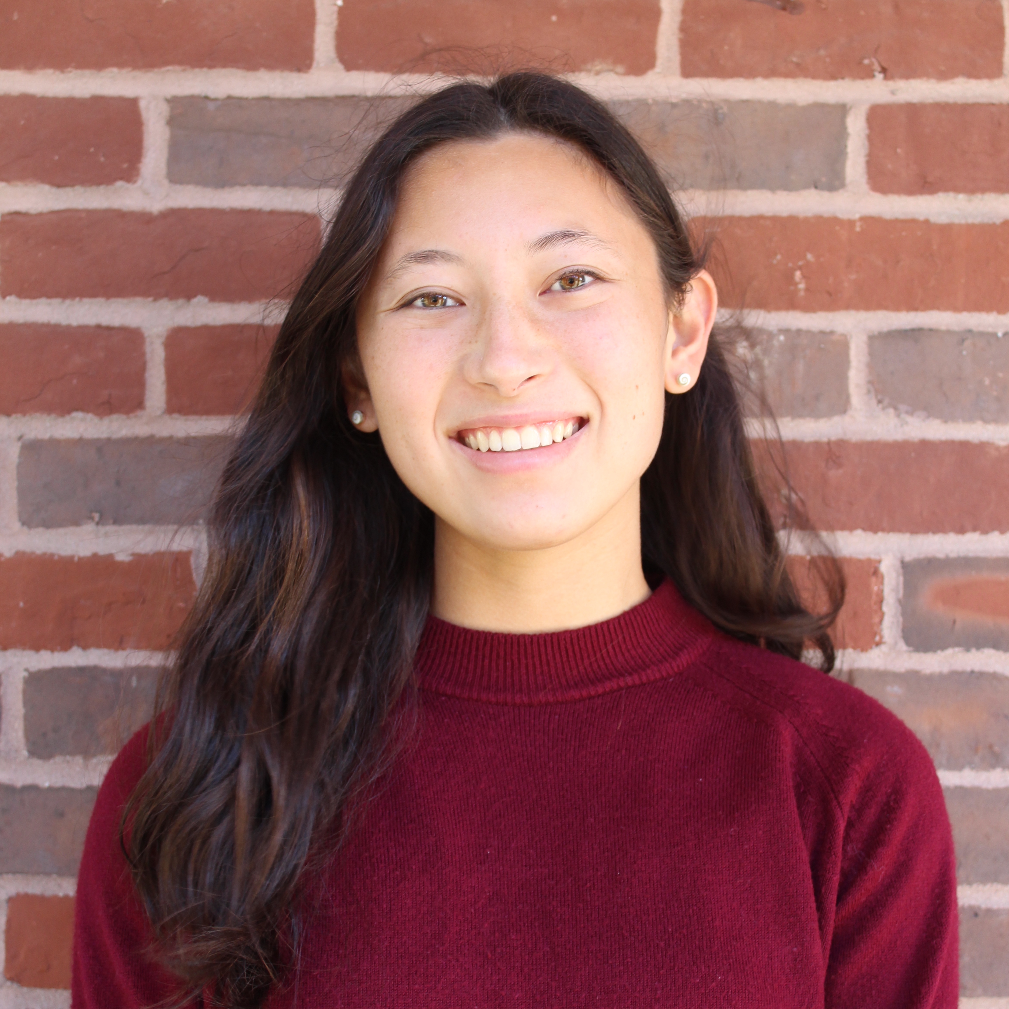 BSU Student Jasmine Won looks at camera and smiles. She is wearing a red sweater and standing against a brick wall