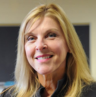 Dr. Lisa Battaglino smiling with medium length blonde hair in front of a classroom chalk board