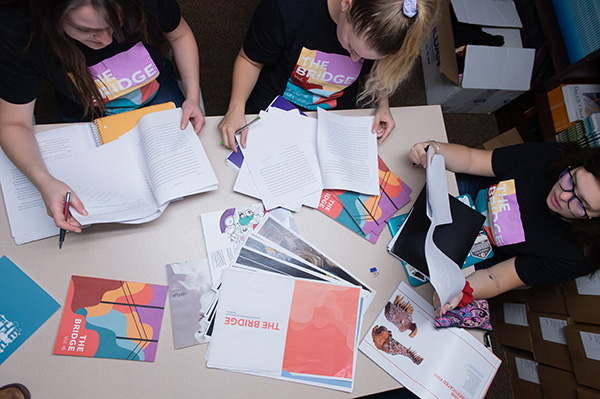 View from above a table where 3 BSU students review writing to include in The Bridge publication