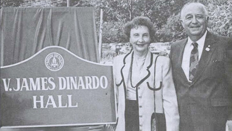 James and Norene DiNardo stand next to a sign saying &quot;V. James DiNardo Hall&quot;