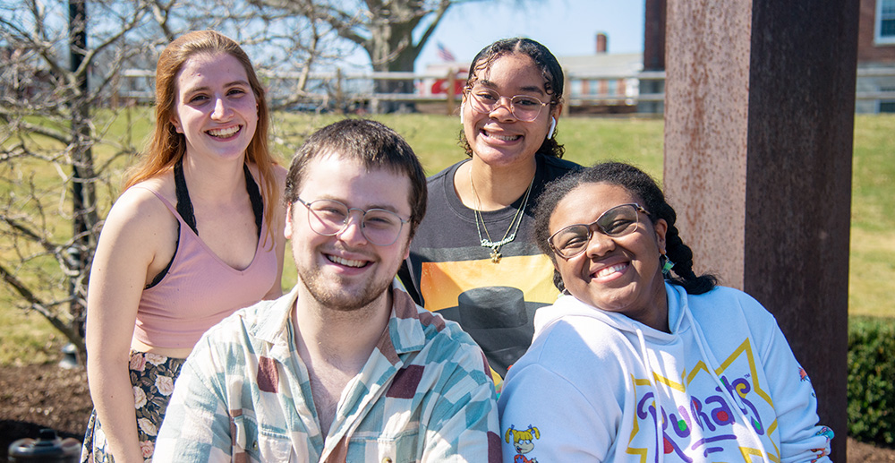 A group of four smiling BSU students outside on a sunny day