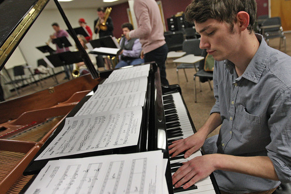 male student playing piano with 5 other students playing brass instruments in background