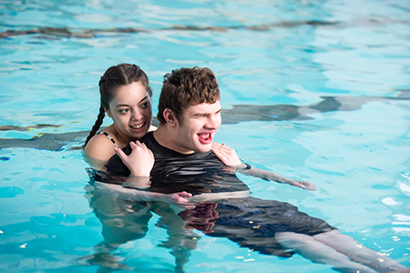 A BSU student helps a youngster swim in a pool.