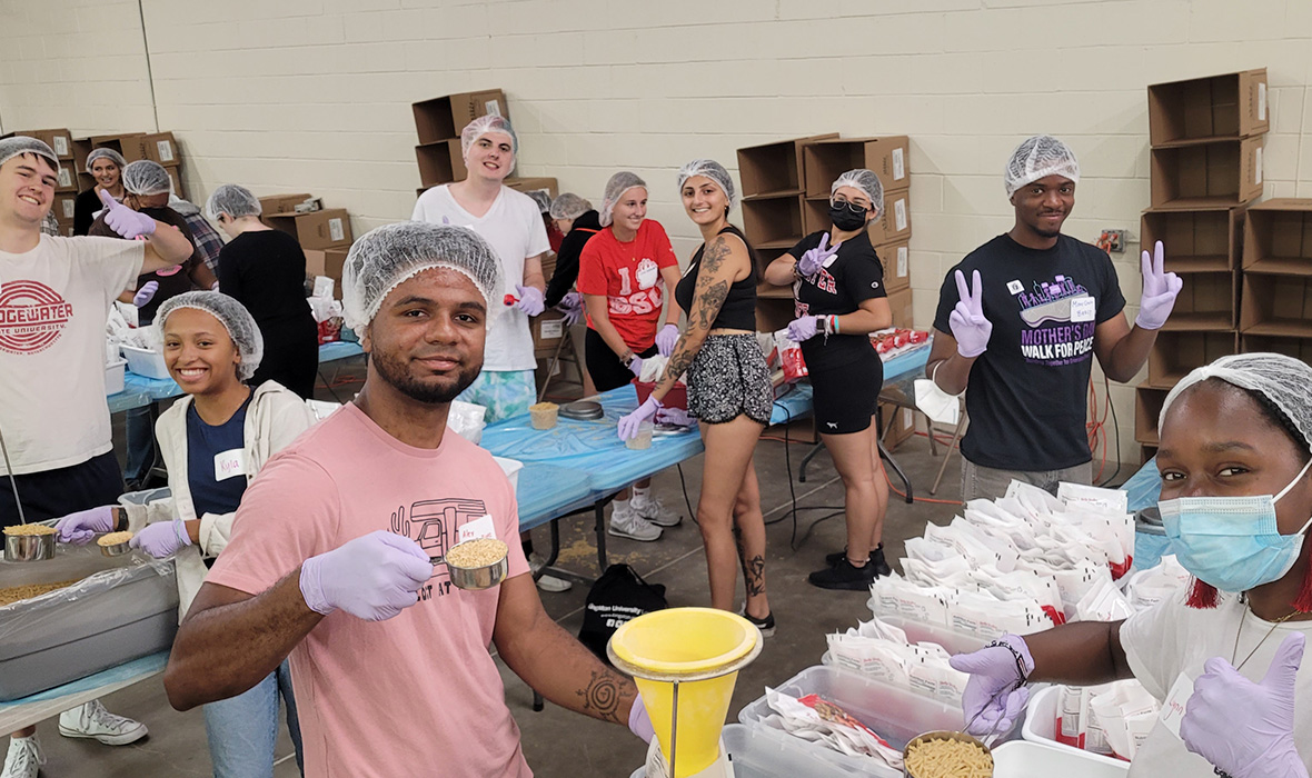A group of students preparing food packages smile for the camera and flash thumbs up