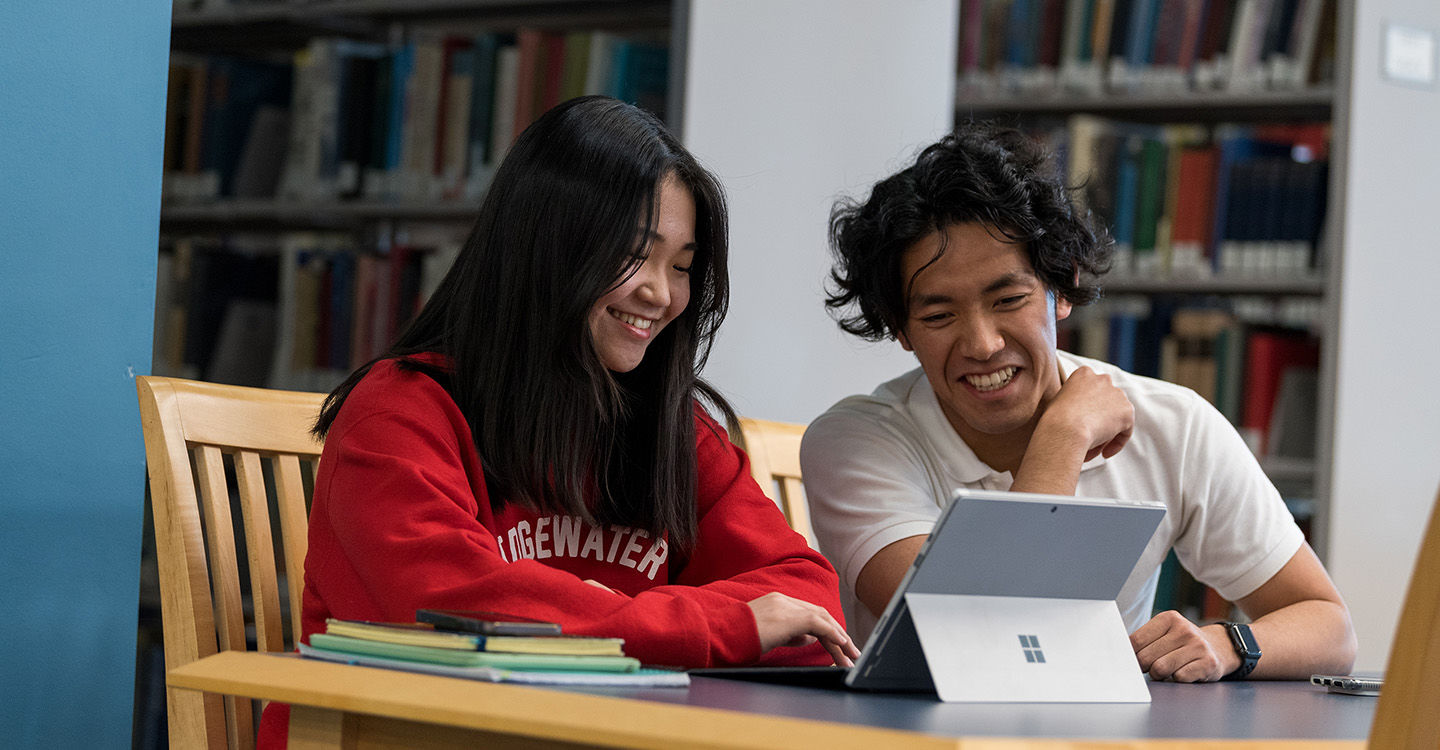 Two students smiling and working on a tablet in the library