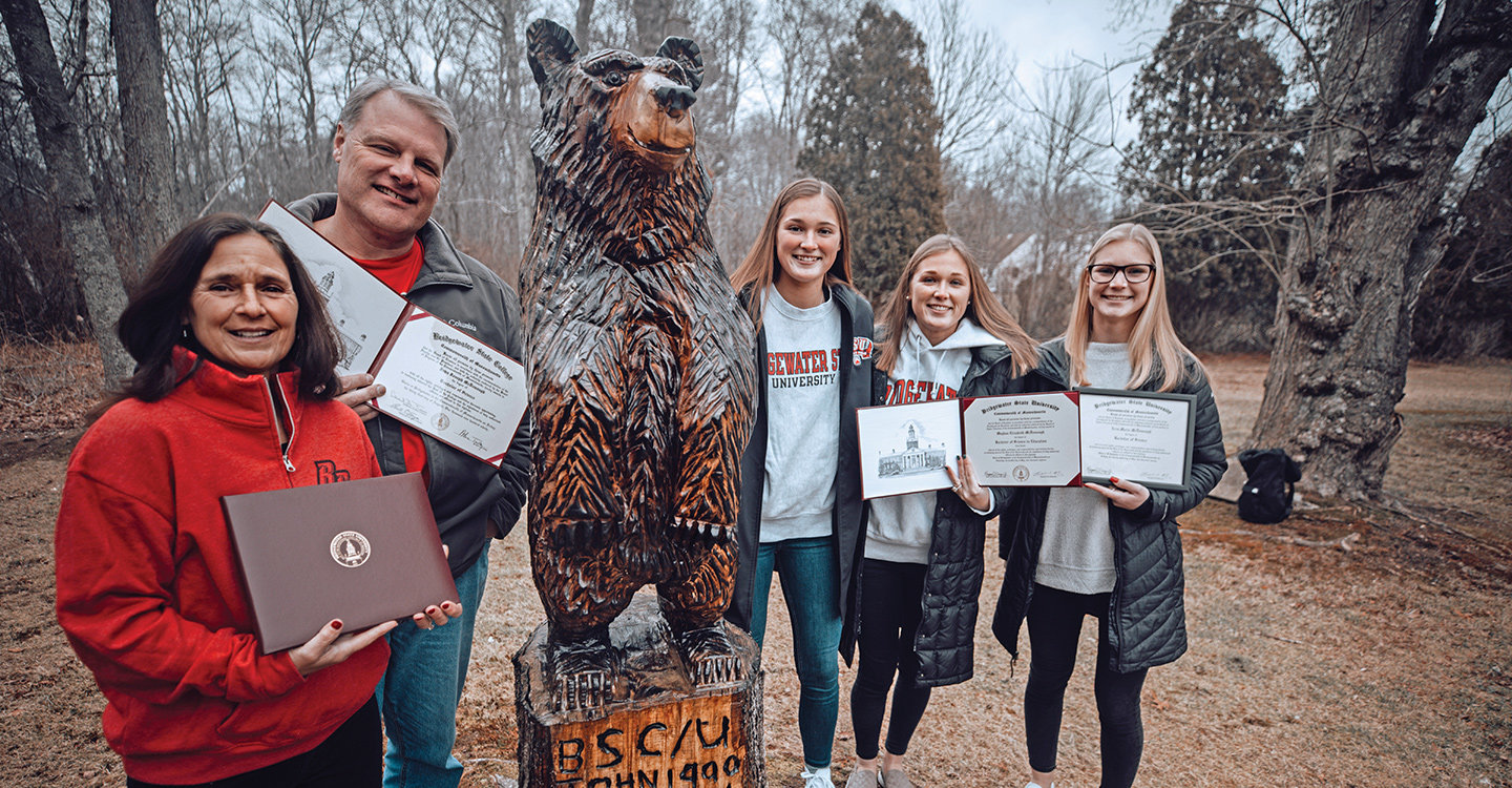 The McDonough Family Show their diplomas while posing next to their bear statue