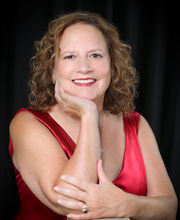Carrie Kulick-Clark smiling with medium length curly brown hair and wearing a sleeveless v-neck red dress