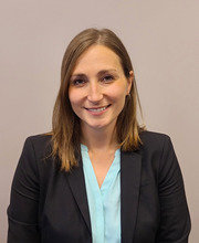 headshot photo of Jaclyn Cowell with shoulder length light brown straight hair wearing a black blazer over a light blue blouse