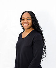 Jasmine Black smiling with long black curly hair and wearing a long sleeve v-neck black top