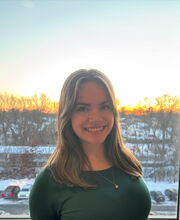 Olivia Blum smiling with medium length straight brown hair and wearing  a long sleeve dark green jersey