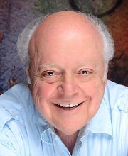 Paul D'Angelo smiling with balding short wavy gray hair and wearing a light blue button up shirt