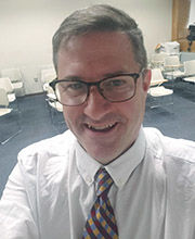 headshot photo of Scott Gagnon in a classroom with short gray hair wearing glasses, a white button-down shirt and a red, blue and yellow check tie