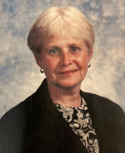 Sheila McKenna smiling with with short gray hair and wearing a black blazer over a black and white floral top