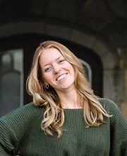 Anna Lofstrom smiling with long dirty-blonde hair and wearing a forest green long sleeved sweater