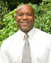 Anthony Ervin, smiling and bald with closely trimmed mustache and goatee, wearing a white button down shirt with a gold and light blue paisley tie