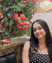 Saifi Zafar smiling with long straight dark hair and wearing a navy polka dot strapless top sitting in a booth next to greenery and flowers