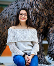 Paulina Aguilar Delgado, '23, smiling and sitting at the base of the bronze bear statue outside Rondileau Student Union