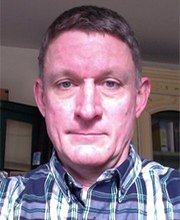 headshot photo of professor Andrew Armstrong with short greyish brown hair wearing a blue, white and green plaid button down shirt with collar