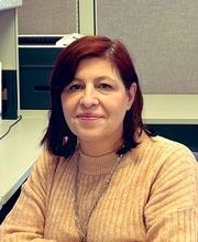 Elizabeth Magalhaes with shoulder length dark brown hair with red highlights wearing an oatmeal colored long sleeve sweater  
