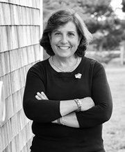 Lisa Rafferty standing next to a shingled building with grass and trees in background