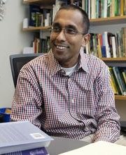 Dr. Thilina Surasinghe sitting at his office desk with bookshelves in background