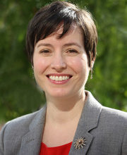 headshot photo of Dr. Sarah Wiggins smiling with short dark brown hair wearing a red blouse under a gray blazer with a sun pin on the lapel