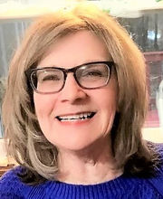 Donna Abelli smiling with medium length dirty blonde hair wearing black rim glasses and a purple sweater