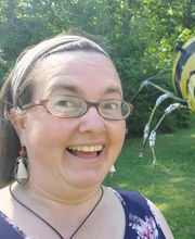 Lisa Boragine smiling with medium length straight brown hair and wearing brown rim glasses and a sleeveless navy blue top with pink and white flowers