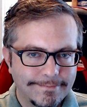 headshot photo of Dr. Richard Brabander with short dark brown/grey hair, mustache and goatee wearing black rim glasses and grey collared shirt