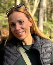Kristen Buchanan smiling with long light brown hair and wearing a black vest over a long sleeve green top