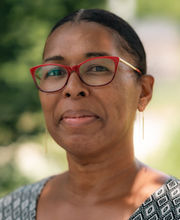 Dr. Wendy Champagnie Williams smiling with black hair pulled back in a low bun wearing red rim glasses and a v-neck green top with white and green diamond pattern