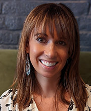 headshot photo of Cynthia Drake smiling with medium length light brown hair and wearing a white v-neck blouse with black flowers print