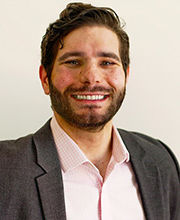 headshot photo of Dr. Kevin Duquette smiling with brown hair, mustache and beard wearing a gray blazer over a pink button down shirt