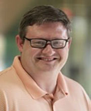 Dr. Jason Edwards smiling with short brown hair and wearing brown rim glasses and a peach colored polo shirt