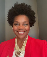 Headshot photo of Elaine Gatewood smiling with short black curly hair wearing a red blazer over a white v-neck blouse and a layered pearl necklace