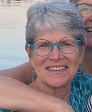 headshot photo of Dr. Susan Eliason smiling with short gray hair, blue rimmed glasses and an aqua blue top